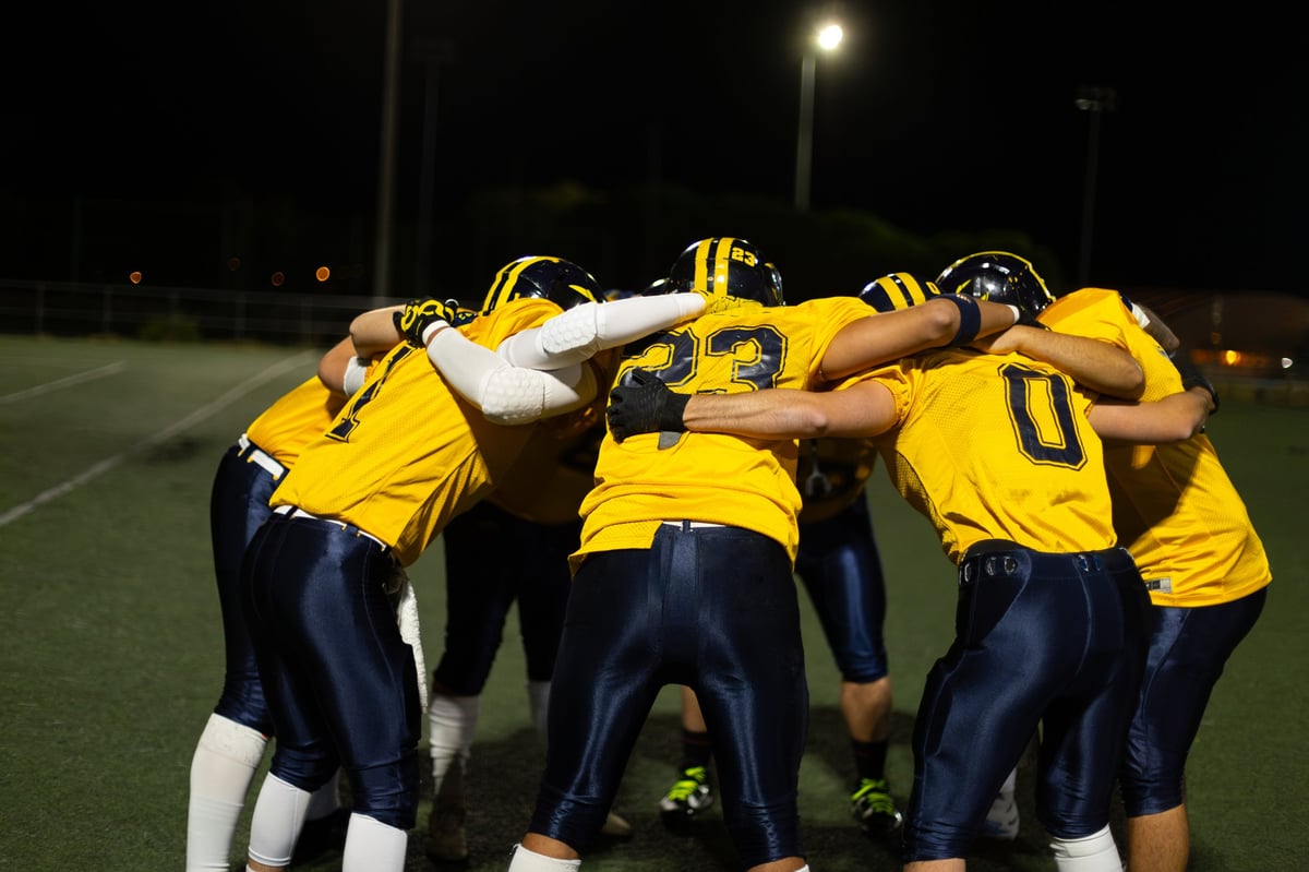 Players forming a huddle, strategizing on the field during a game under floodlights