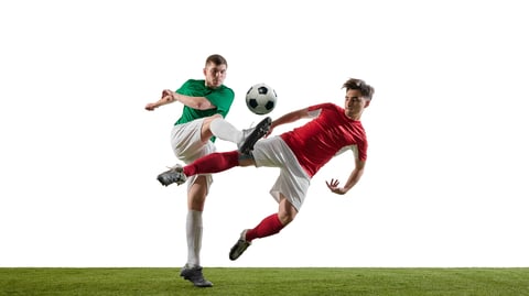 Soccer players in green and red jerseys kicking ball in midair during intense match on grass. Concept of athleticism, rivalry, and skillful sports performance.