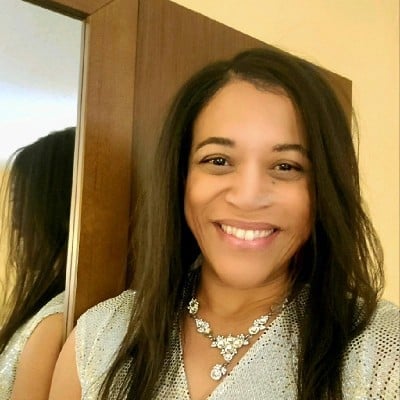 Smiling woman with long dark hair wearing a light-colored top and decorative necklace
