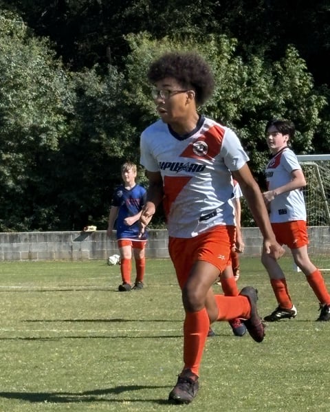Young soccer player in red and white uniform running with ball during youth soccer match on grass field with teammates in background