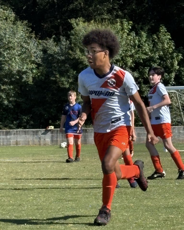 Young soccer player in red and white uniform running with ball during youth soccer match on grass field with teammates in background