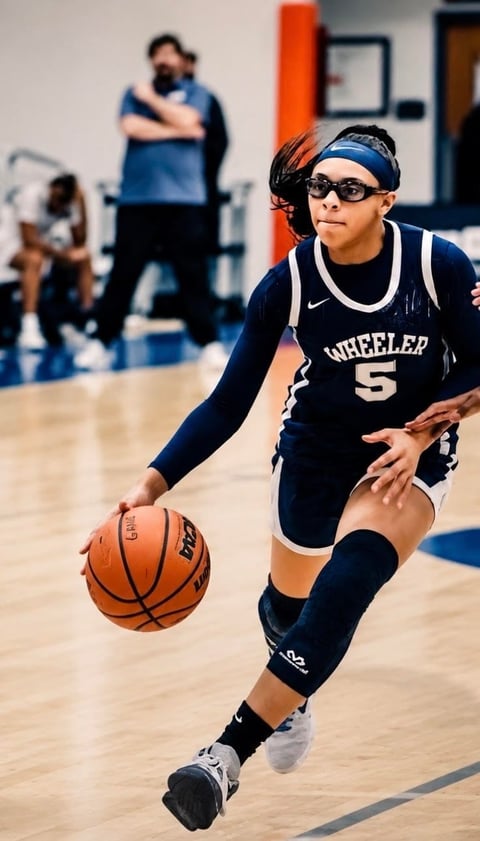 Young female basketball player in Wheeler jersey number 5 dribbling ball on indoor court during game