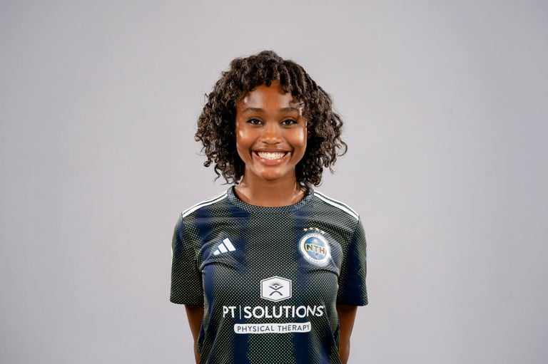 Smiling young woman with curly dark hair wearing a dark green PT Solutions Physical Therapy sports jersey against a light gray background